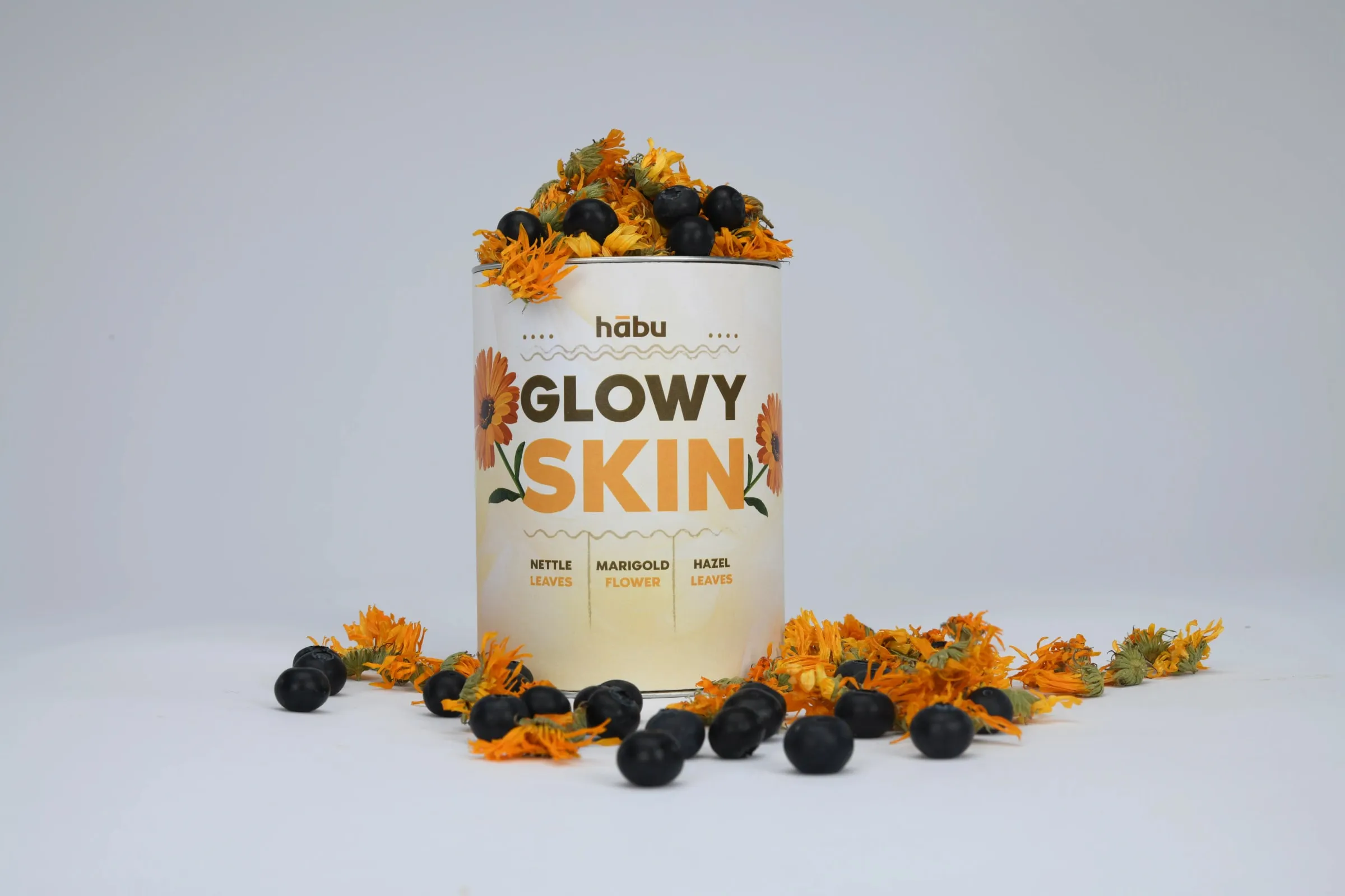 A Glowy Skin tin topped with marigold petals and blackberries.
