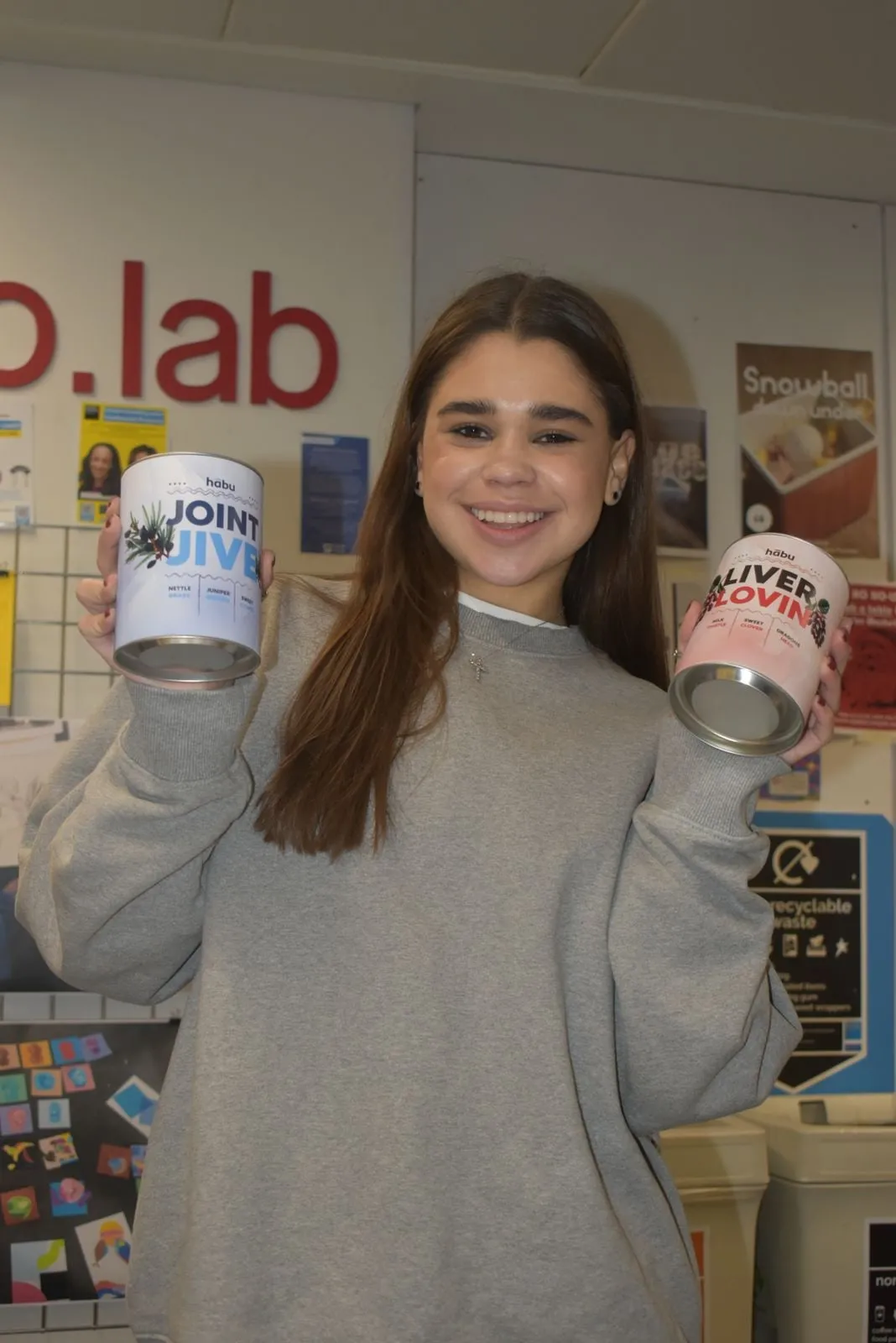 A student holding up a Joint Jive tin and a Liver Lovin' tin and smiling.