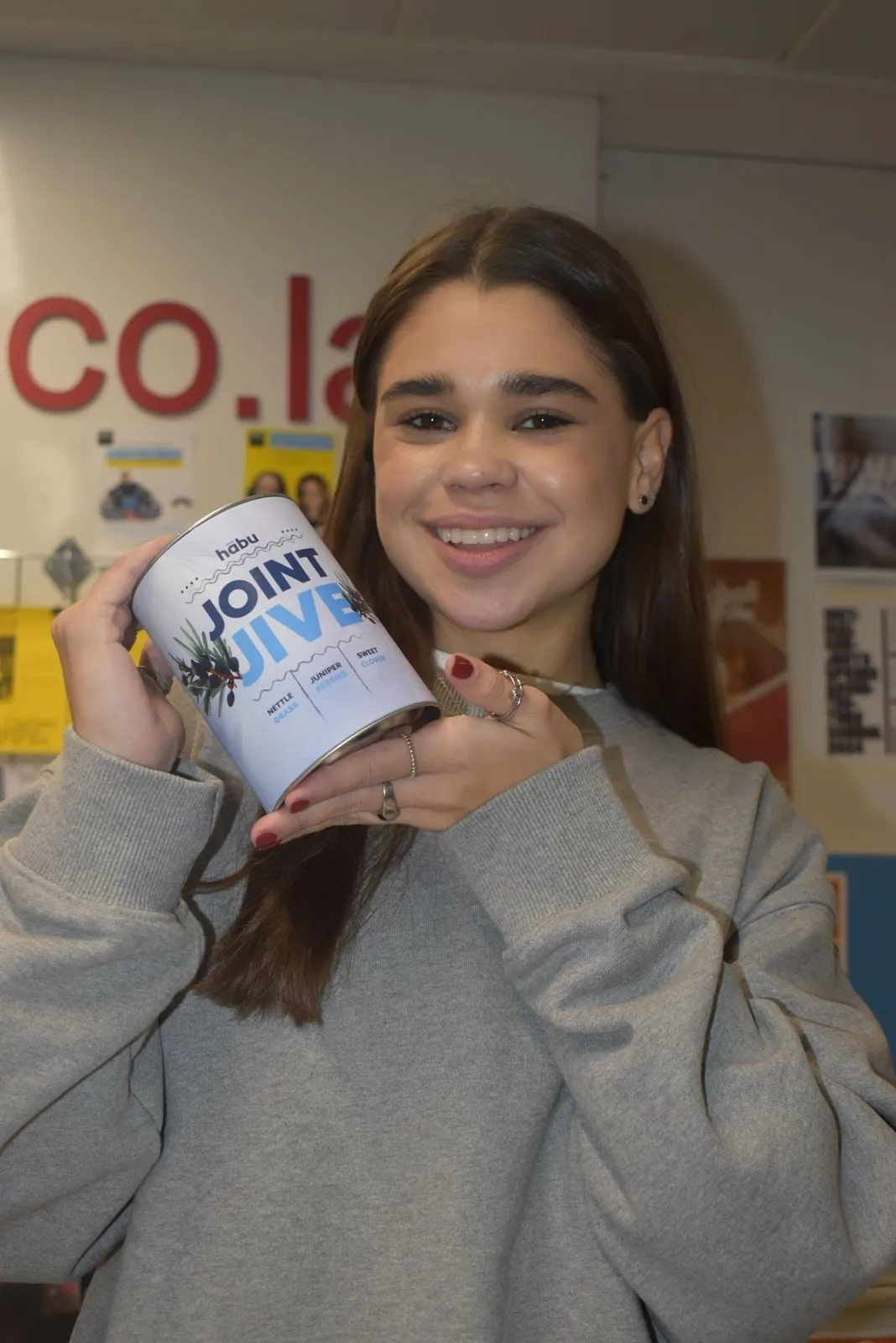A student smiling and holding a Joint Jive tin close to her face.