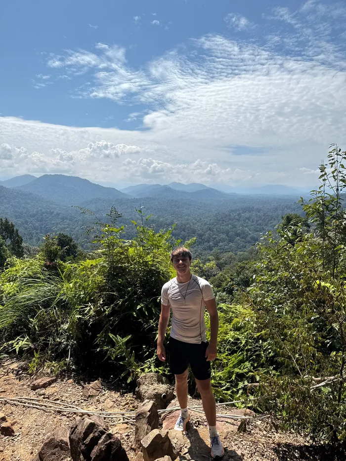 Denis standing on a rocky lookout above green mountains.