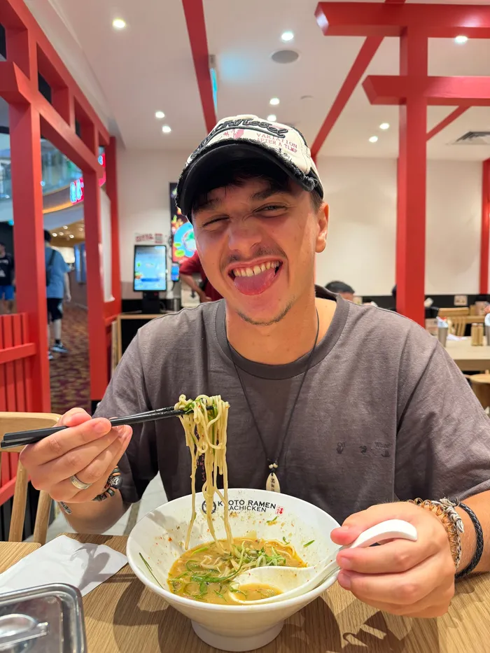 Denis laughing over a bowl of noodles, chopsticks in hand.