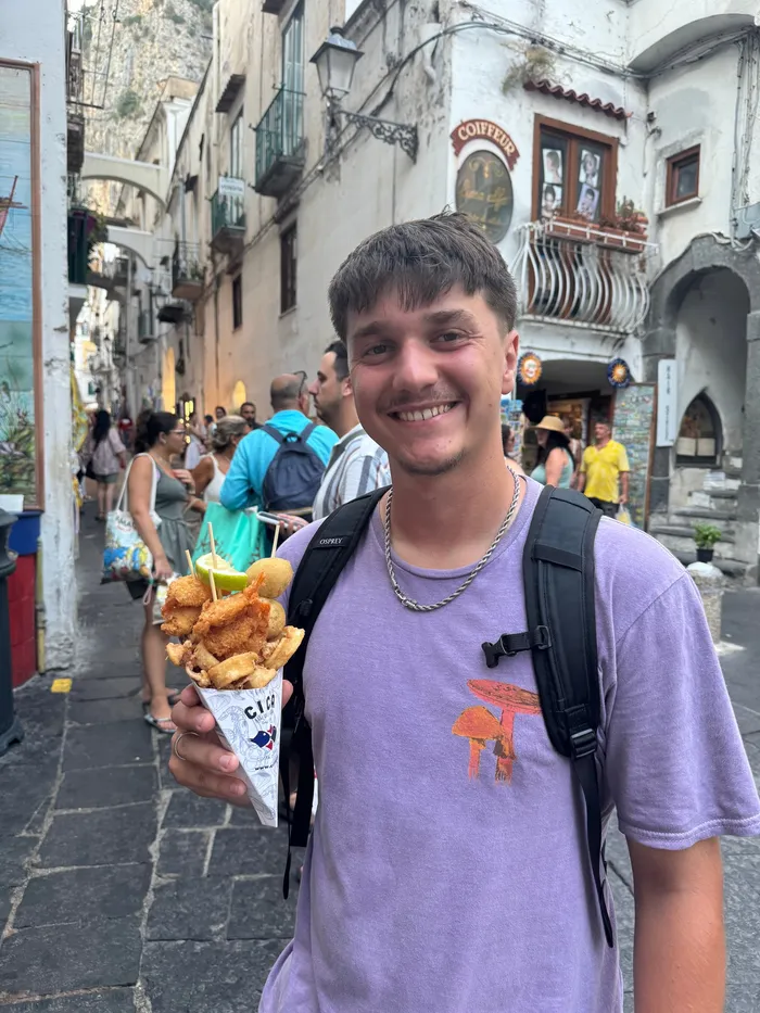 Denis holding a cone of food in a narrow old street.