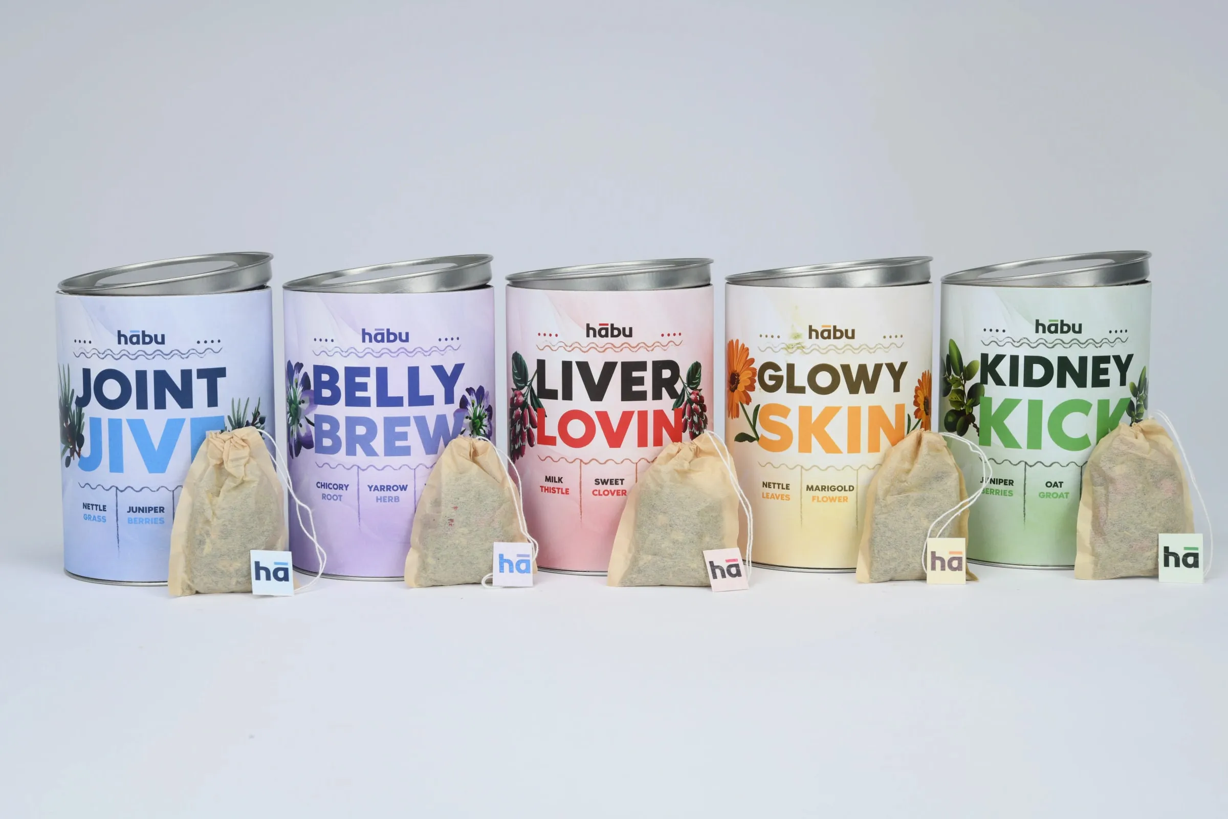 All five Habu tins standing in a row, Joint Jive, Belly Brew, Liver Lovin', Glowy Skin and Kidney Kick, each with a tea bag beside it.